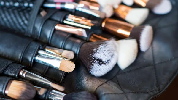 Close-up of professional makeup brushes with rose gold and silver handles arranged in a black leather roll.