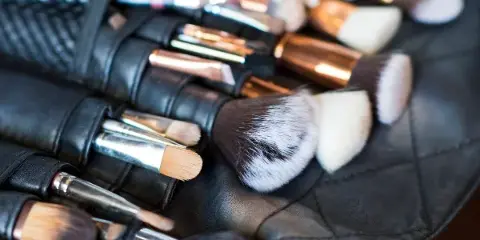 Close-up of professional makeup brushes with rose gold and silver handles arranged in a black leather roll.