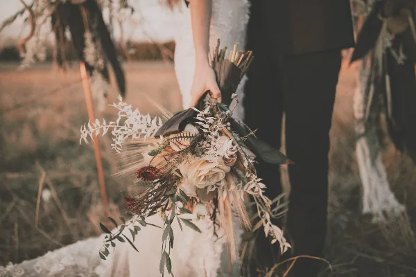 A bride and groom holding a rustic wedding bouquet in a field.