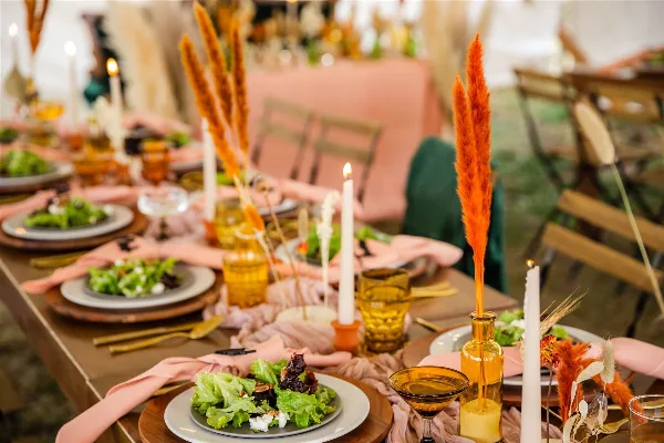 A long dining table set for a formal event with plates of salad, candles, and dried floral arrangements.