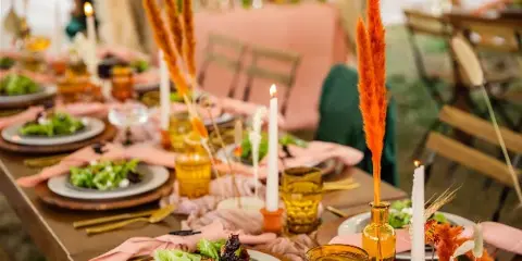 A long dining table set for a formal event with plates of salad, candles, and dried floral arrangements.