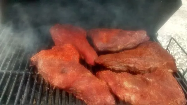 Large cuts of seasoned meat smoking on a grill grate with visible smoke.