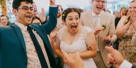 A candid documentary photograph of a bride and groom laughing and celebrating with their wedding guests.