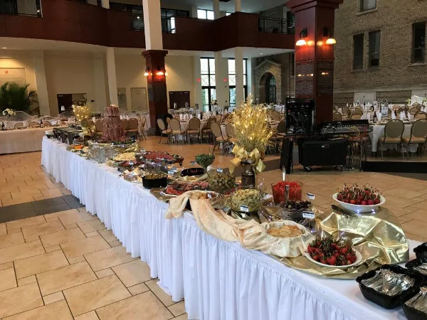 A catering buffet table with various food items, chafing dishes, and decorations set up in an event venue.