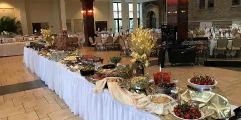 A catering buffet table with various food items, chafing dishes, and decorations set up in an event venue.