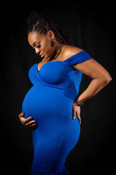 Studio maternity portrait of a woman in a blue dress against a black background