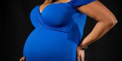 Studio maternity portrait of a woman in a blue dress against a black background
