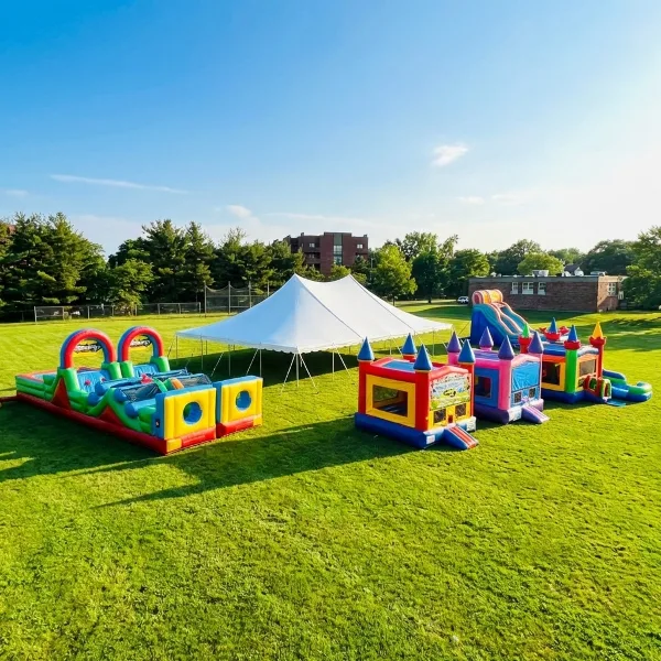 A white event tent and several colorful inflatable bounce houses and water slides set up on a green lawn.
