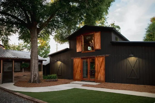 Exterior view of a dark barn-style event venue with wooden sliding doors and a cottage structure.