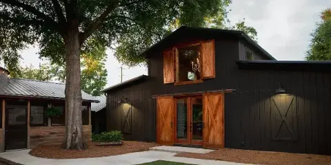 Exterior view of a dark barn-style event venue with wooden sliding doors and a cottage structure.