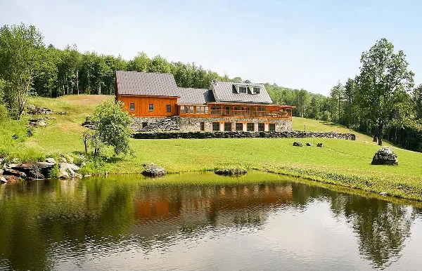 Exterior view of a large stone and wood farmhouse with a pond in the foreground