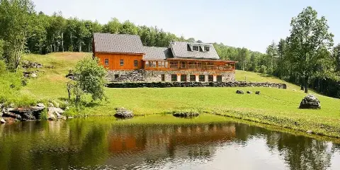 Exterior view of a large stone and wood farmhouse with a pond in the foreground