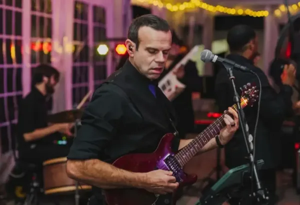 A male musician playing an electric guitar on stage during a live performance.