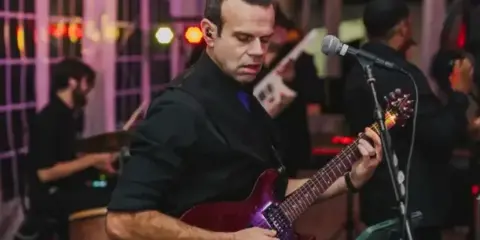 A male musician playing an electric guitar on stage during a live performance.