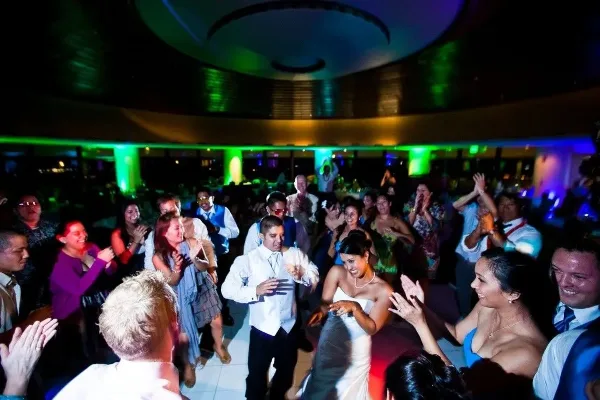 A crowded wedding reception dance floor with colorful lighting and guests dancing.