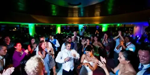 A crowded wedding reception dance floor with colorful lighting and guests dancing.