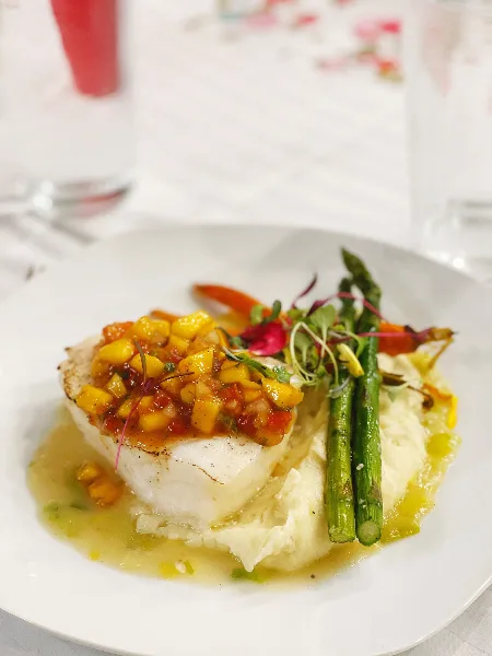A plated dish of seared white fish topped with mango salsa, served with mashed potatoes and grilled asparagus on a white plate.