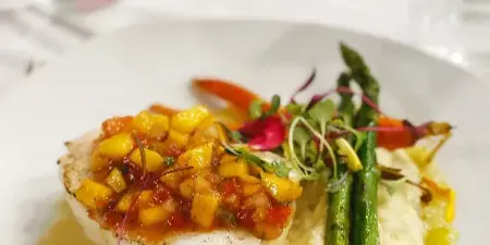 A plated dish of seared white fish topped with mango salsa, served with mashed potatoes and grilled asparagus on a white plate.