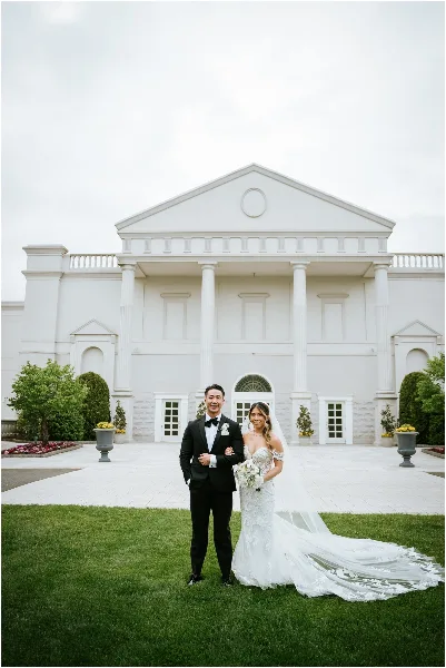 A bride and groom standing on the lawn in front of the white Palladian-style mansion facade of The Palace at Somerset Park.
