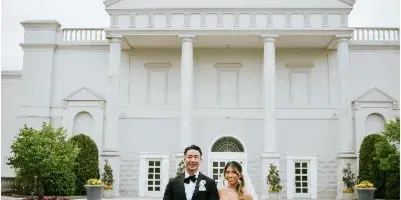 A bride and groom standing on the lawn in front of the white Palladian-style mansion facade of The Palace at Somerset Park.