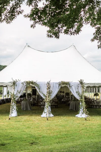 A white event tent with floral columns and table settings on a grassy lawn.