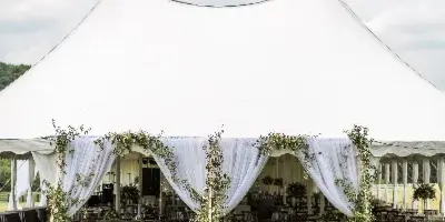A white event tent with floral columns and table settings on a grassy lawn.