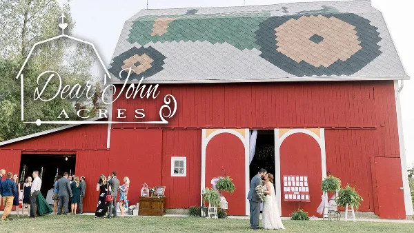 Exterior view of a red barn wedding venue with a bride and groom kissing in front of the open doors.
