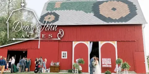 Exterior view of a red barn wedding venue with a bride and groom kissing in front of the open doors.