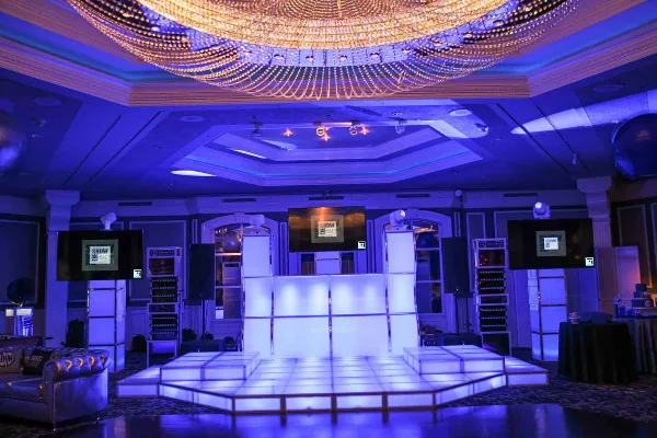 A professional event venue featuring a large illuminated dance floor, DJ equipment, and stage lighting.
