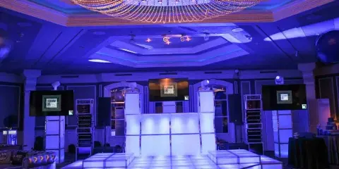 A professional event venue featuring a large illuminated dance floor, DJ equipment, and stage lighting.