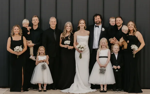 A wedding party posing for a group photo in front of a dark industrial metal wall.