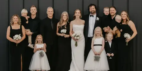 A wedding party posing for a group photo in front of a dark industrial metal wall.