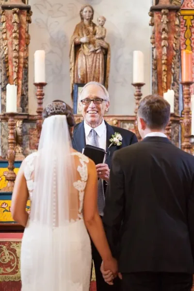 Father Jerry Bellamy officiating a wedding ceremony between a bride and groom in a church setting.