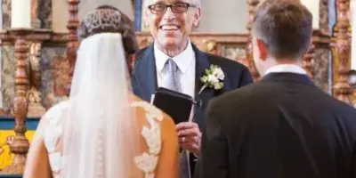 Father Jerry Bellamy officiating a wedding ceremony between a bride and groom in a church setting.