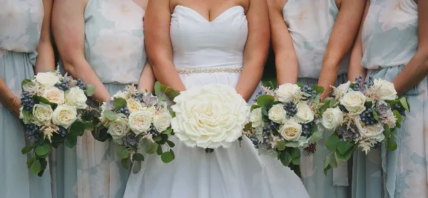 A bride and bridesmaids holding white and blue floral bouquets with eucalyptus greenery.