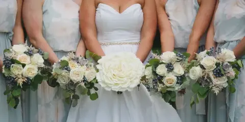 A bride and bridesmaids holding white and blue floral bouquets with eucalyptus greenery.