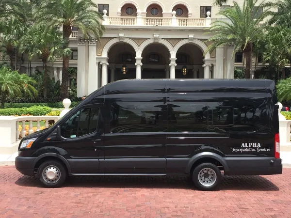 A black Alpha Transportation Services Sprinter van parked on a brick driveway in front of a luxury hotel or venue entrance.
