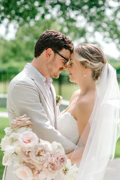 A bride and groom standing close together outdoors, with the bride holding a large bouquet of white and pink roses.