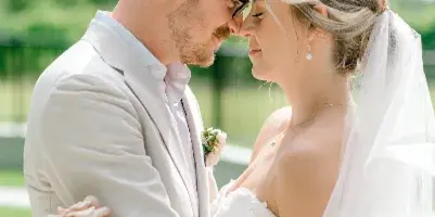 A bride and groom standing close together outdoors, with the bride holding a large bouquet of white and pink roses.