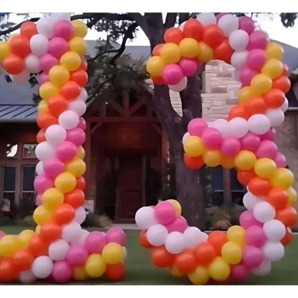 Large outdoor balloon letters in pink, orange, yellow, and white arranged on a lawn in front of a house.
