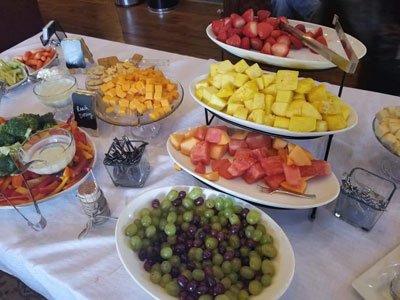 A catering table featuring multiple bowls of fresh fruit including grapes, watermelon, pineapple, and cantaloupe.