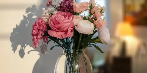 A floral arrangement of pink and white roses and other blooms in a clear glass vase on a wooden table.