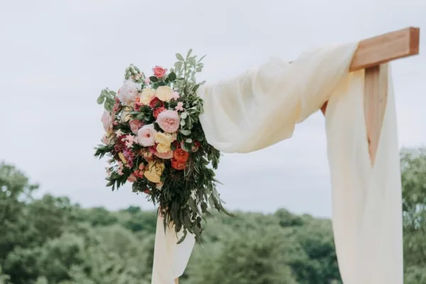 A wooden wedding arch decorated with a large floral arrangement and flowing white fabric.