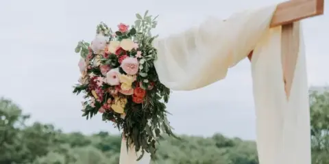 A wooden wedding arch decorated with a large floral arrangement and flowing white fabric.