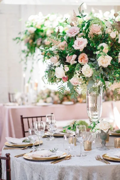 Wedding table centerpiece with pink and white roses, greenery, and tall glass vase at a styled reception table