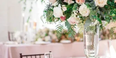 Wedding table centerpiece with pink and white roses, greenery, and tall glass vase at a styled reception table