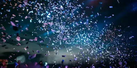 A large crowd of people at an event with confetti falling from the ceiling.