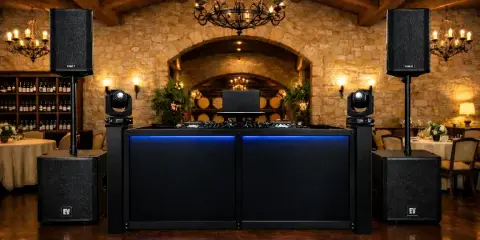 A professional DJ booth with a mixer, speakers, and lighting equipment set up in a rustic stone-walled wedding venue.