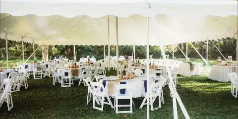 A large white event tent set up on a grassy lawn containing multiple round tables with white tablecloths and white folding chairs.