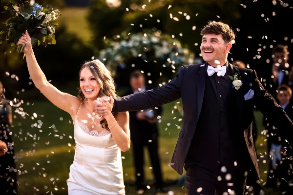 A bride and groom laughing and celebrating with confetti in the air during a wedding.
